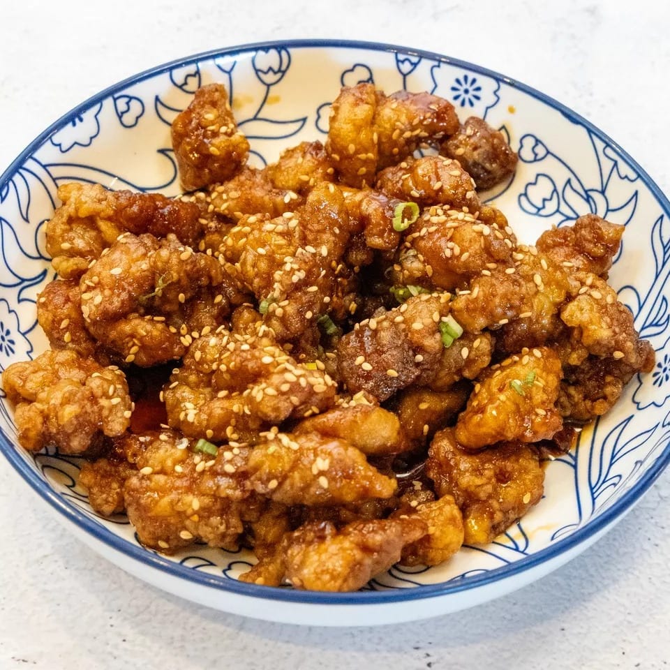Crispy sesame chicken with green onions in a blue and white patterned bowl.