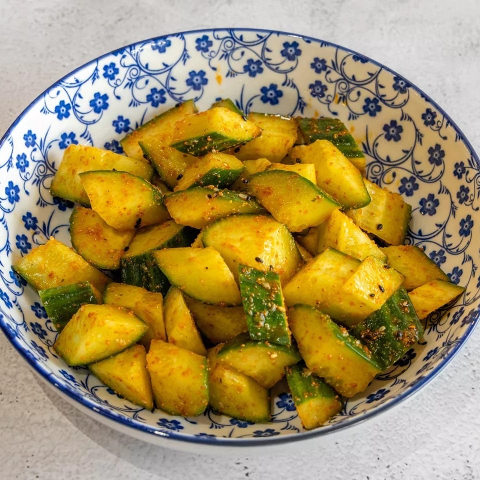 A blue and white patterned bowl filled with seasoned cucumber slices, sprinkled with spices and sesame seeds.
