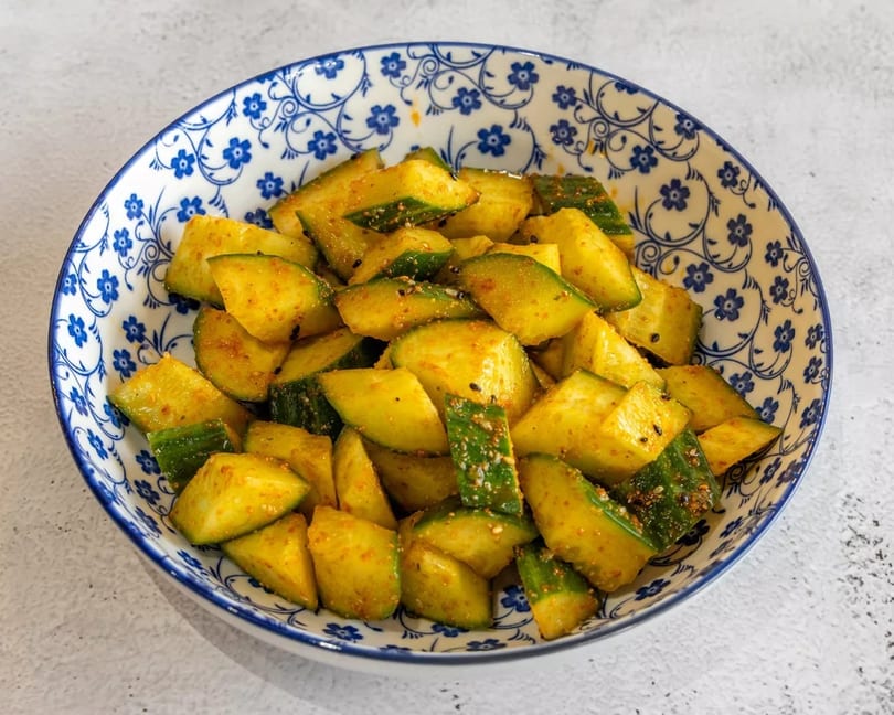 A blue and white patterned bowl filled with seasoned cucumber slices, sprinkled with spices and sesame seeds.