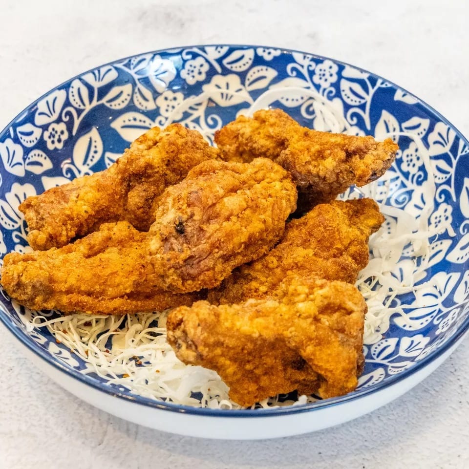 Crispy fried chicken wings served on a bed of shredded cabbage in a blue and white patterned bowl.