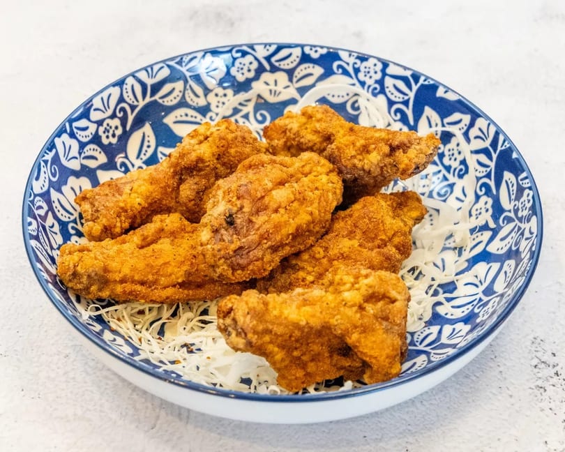Crispy fried chicken wings served on a bed of shredded cabbage in a blue and white patterned bowl.