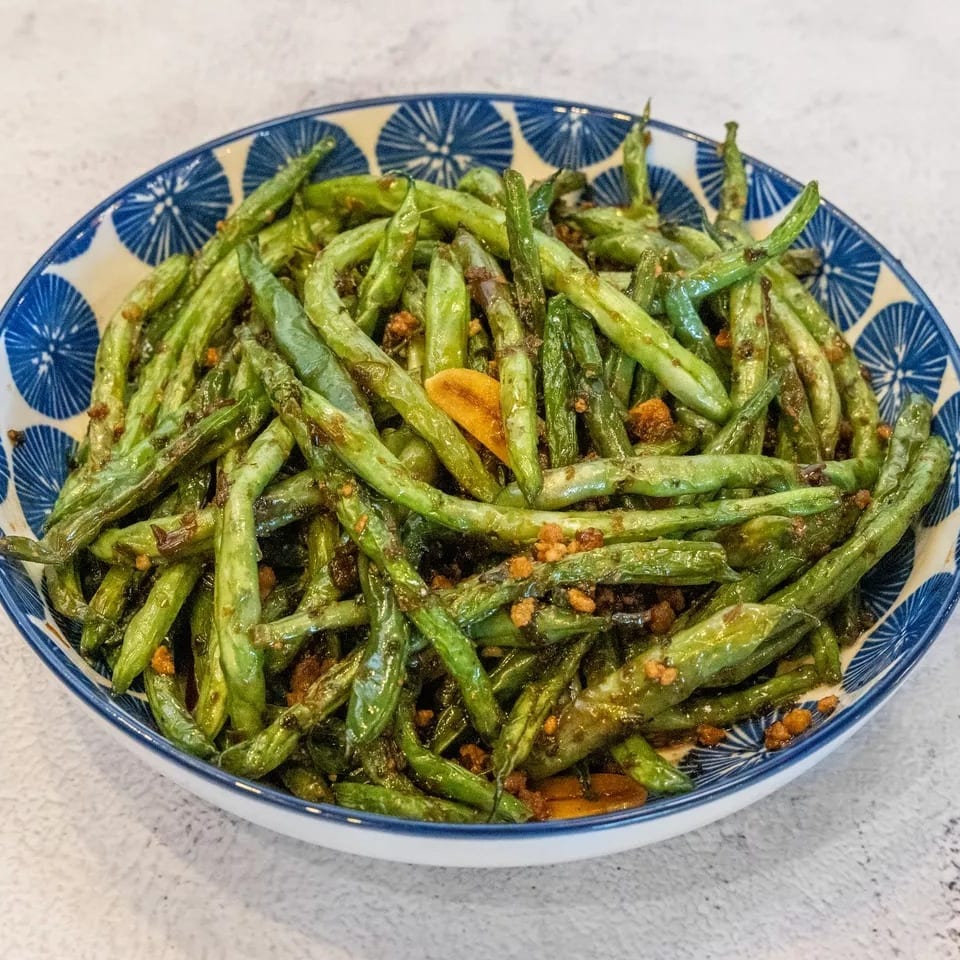 A blue and white patterned bowl filled with stir-fried green beans and garlic.
