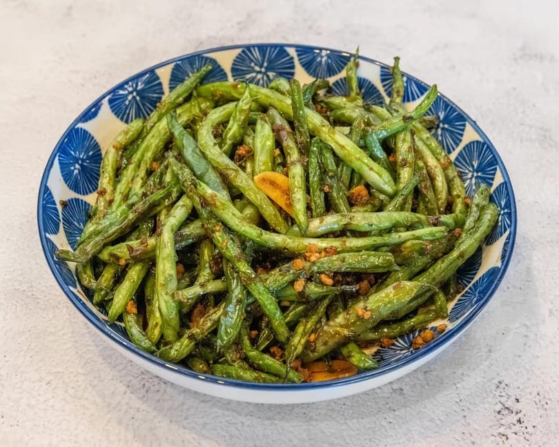 A blue and white patterned bowl filled with stir-fried green beans and garlic.